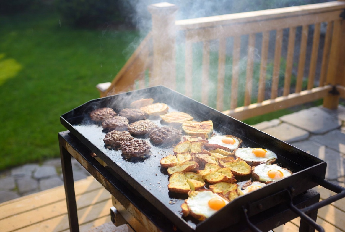 Smash burgers, eggs, and breakfast potatoes cooking on a Blackstone griddle on a backyard deck